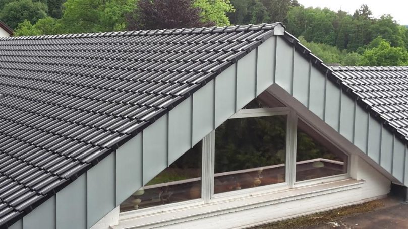 Zweiflügelige Dachkonstruktion mit schwarzen Ziegeln und großen Fenstern.