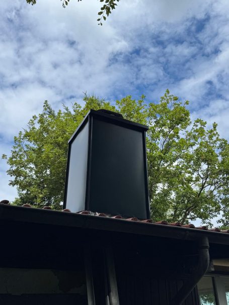 Schwarzer Schornstein auf einem Dach mit Stehpfalz